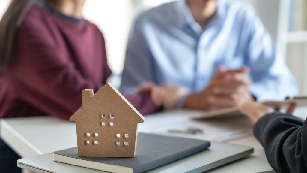Couple en rendez-vous avec un courtier pour un crédit immobilier, maquette de maison sur le bureau